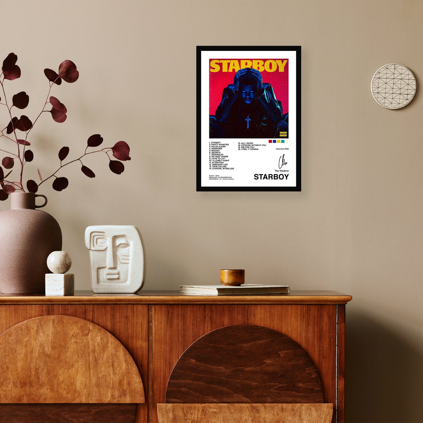 A framed poster of "starboy" mounted on a beige wall above a wooden sideboard with decorative items